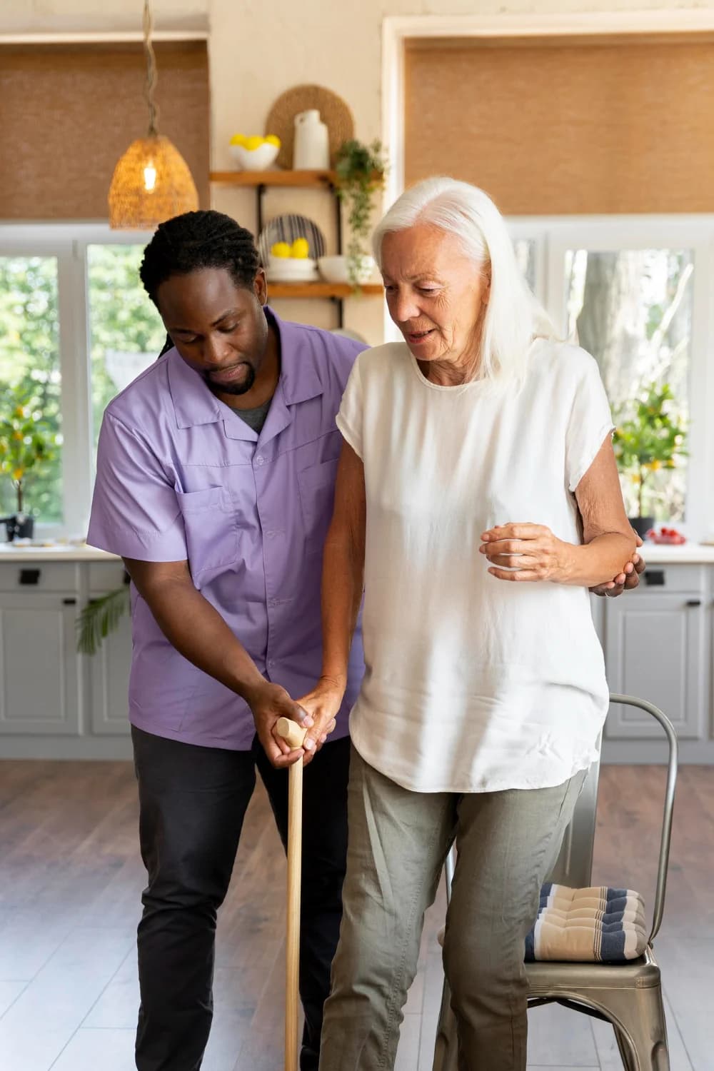 A carer helping an adult prepare food together in a warm sunlit kitchen